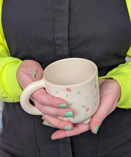 Person holding a ceramic mug with floral patterns against a dark background
